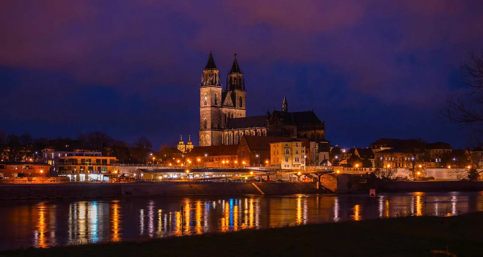 Magdeburger Dom bei Nacht an der Elbe, die Lichter der Altstadt spiegeln sich im Wasser